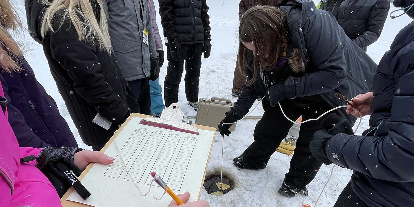 Students taking a sample out of a lake in the middle of winter
